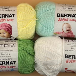 以下が含まれることがあります： 黄色、ミントグリーン、緑、白のBernat Softee Babyの毛糸が6玉。各玉は140gです。この毛糸はアクリル製で、ベビープロジェクトに適しています。パッケージには赤ちゃんの写真が掲載されています。
