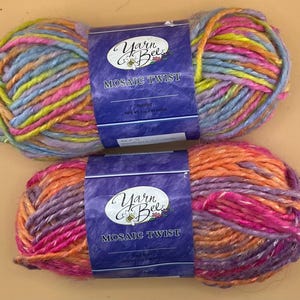 Könnte beinhalten: Zwei Stränge Yarn Bee Mosaic Twist Garn in leuchtenden Farben. Einer zeigt eine Mischung aus Blau, Gelb, Rosa und Orange, der andere Orange-, Rosa- und Lilatöne. Jeder Strang hat ein Etikett mit der Aufschrift "Mosaic Twist".