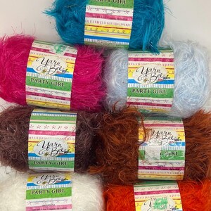 Könnte beinhalten: Eine Auswahl an Yarn Bee Party Girl Garnknäueln in verschiedenen Farben, darunter Türkis, Pink, Weiß, Braun und Orange. Jedes Knäuel ist mit einem Etikett mit dem Markenlogo und Produktinformationen versehen. Das Garn hat eine flauschige Textur.