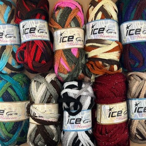 May include: A selection of Ice Yarns Flamenco yarn skeins in various colours. The skeins display shades of teal, red, pink, and brown, with metallic threads. Each skein is labelled with "Ice Yarns Flamenco".