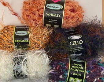 May include: Five skeins of textured novelty yarn with paper labels. The top skein is orange and red labelled Whimsy. Below are orange and yellow Radiance, dark blue and brown Cello, white Cello, and a purple, teal, and white Spirits yarn skein.