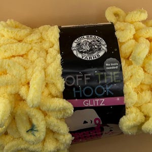 May include: A skein of yellow "Off The Hook Glitz" yarn by Lion Brand Yarns. The yarn is a soft, looped texture, with a label that reads "No tools needed!" The yarn is a bright, sunny yellow color.