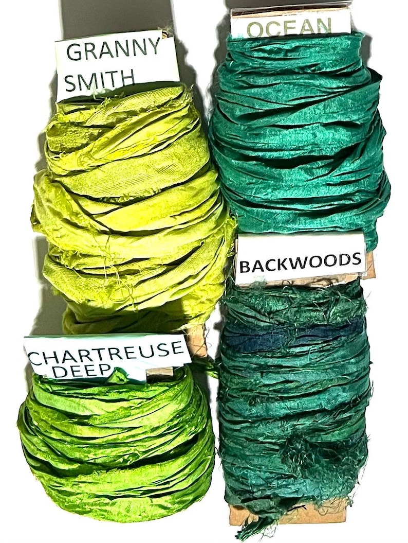 K&ouml;nnte beinhalten: Vier Spulen aus zerknittertem Seidenband in Gr&uuml;nt&ouml;nen. Die Etiketten tragen die Aufschriften Granny Smith, Ocean, Backwoods und Chartreuse Deep. Jede Spule besteht aus strukturiertem Stoff mit ausgefransten Kanten, der um einen Kern gewickelt ist.