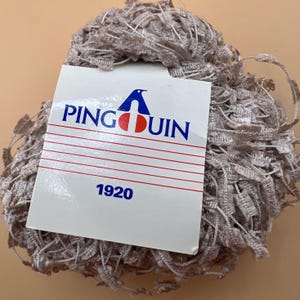 Könnte beinhalten: Eine Spule hellbraunen Garns mit einem weißen Etikett, auf dem "PINGOUIN 1920" steht.