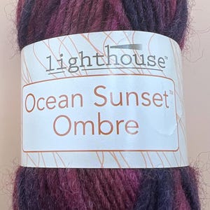 May include: A skein of yarn in a gradient of purple and blue colors. The yarn is labeled "Lighthouse Ocean Sunset Ombre".