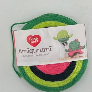 May include: A skein of yarn in green, yellow, black, and pink colors. The yarn is labeled "Red Heart Amigurumi" and "each one makes two".