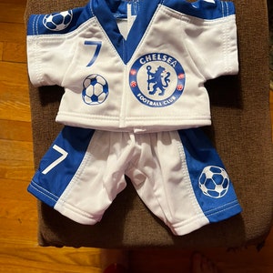 Puede incluir: Camiseta de f&uacute;tbol blanca y azul con el n&uacute;mero 7 y el logotipo del Chelsea Football Club. La camiseta se combina con pantalones cortos blancos y azules a juego.