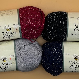 May include: Four skeins of Yarn Bee Glint of Glam yarn. The yarn has a sparkly, chenille-like texture. The colours are burgundy, silver, black, and navy.