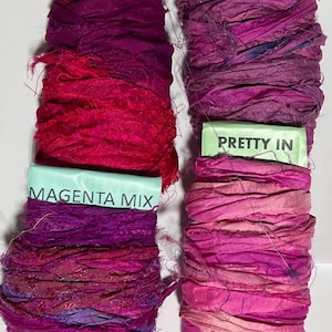 K&ouml;nnte beinhalten: Vier Seidenbandspulen in verschiedenen Rosa- und Violettt&ouml;nen. Die Etiketten tragen die Aufschriften Flamenco, Heliotrope, Magenta Mix und Pretty In. Jede Spule besteht aus ausgefranstem, strukturiertem Stoff auf einem Pappkern.