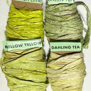 K&ouml;nnte beinhalten: Vier Spulen mit strukturiertem Band in Gr&uuml;n- und Gelbt&ouml;nen. Die Etiketten tragen die Aufschriften Lemon Lime, Green Tea, Mellow Yellow und Dahling Tea. Jede Spule hat einen eigenen Farbton, von leuchtendem Limettengr&uuml;n bis zu blassem Gelb.
