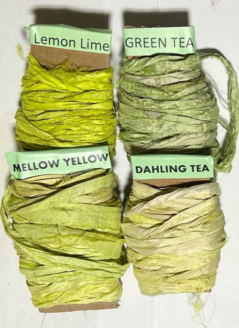 K&ouml;nnte beinhalten: Vier Spulen mit strukturiertem Band in Gr&uuml;n- und Gelbt&ouml;nen. Die Etiketten tragen die Aufschriften Lemon Lime, Green Tea, Mellow Yellow und Dahling Tea. Jede Spule hat einen eigenen Farbton, von leuchtendem Limettengr&uuml;n bis zu blassem Gelb.