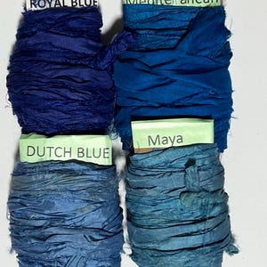 K&ouml;nnte beinhalten: Vier Spulen aus zerknittertem Seidenband in Blaut&ouml;nen. Die obere linke Spule ist mit ROYAL BLUE beschriftet, die obere rechte mit Mediterranean, die untere linke mit DUTCH BLUE und die untere rechte mit Maya auf hellgr&uuml;nem Papier.