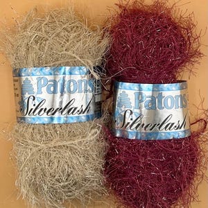 May include: Two skeins of Patons Silverlash yarn. One is a light beige color with silver strands, and the other is a deep burgundy with silver strands. The yarn labels feature the brand name and product name in a blue and silver design.