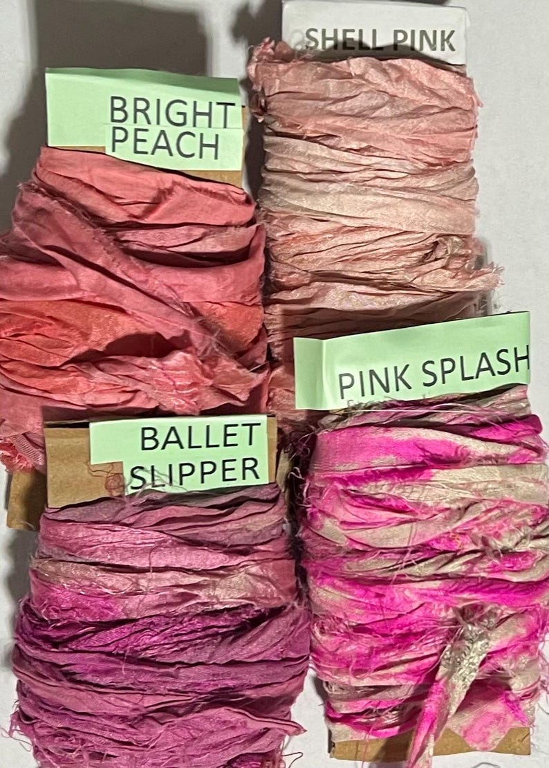 K&ouml;nnte beinhalten: Vier Spulen aus zerknittertem Seidenband in verschiedenen Rosa- und Pfirsicht&ouml;nen. Jede Spule hat ein hellgr&uuml;nes Etikett mit dem Text: Bright Peach, Shell Pink, Ballet Slipper und Pink Splash. Die B&auml;nder haben eine strukturierte, ausgefranste Optik.