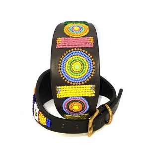 K&ouml;nnte beinhalten: Ein braunes Lederhundekragen mit bunten, geometrischen Perlenmustern. Das Halsband zeigt Kreise, Quadrate und Rechtecke in den Farben Gelb, Orange, Rosa, Blau und Gr&uuml;n.