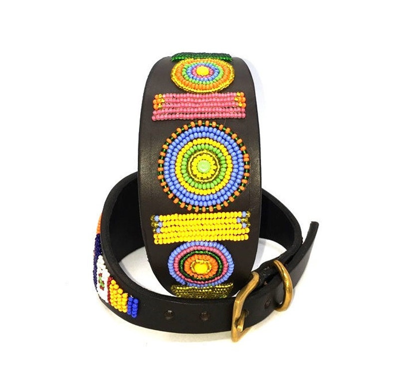 K&ouml;nnte beinhalten: Ein braunes Lederhundekragen mit bunten, geometrischen Perlenmustern. Das Halsband zeigt Kreise, Quadrate und Rechtecke in den Farben Gelb, Orange, Rosa, Blau und Gr&uuml;n.