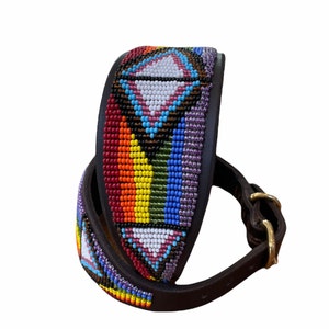 K&ouml;nnte beinhalten: Ein braunes Lederhundekragen mit einem bunten Perlenmuster. Die Perlen sind in einem geometrischen Muster mit einem Regenbogen aus Farben angeordnet, darunter Rot, Orange, Gelb, Gr&uuml;n, Blau und Lila. Das Halsband hat eine Messing-Schnalle.