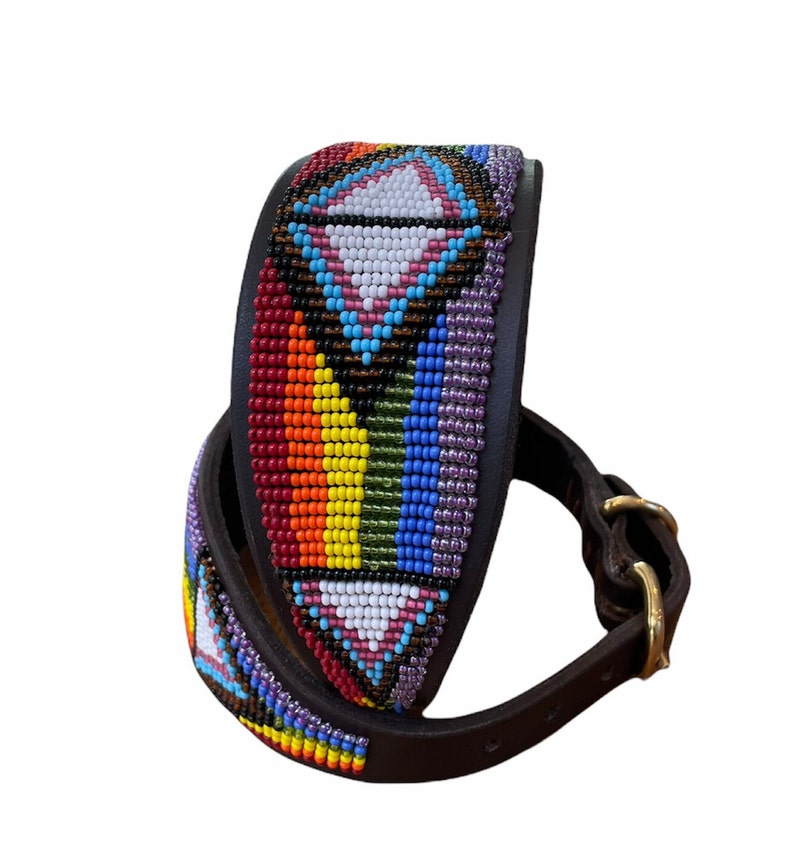 K&ouml;nnte beinhalten: Ein braunes Lederhundekragen mit einem bunten Perlenmuster. Die Perlen sind in einem geometrischen Muster mit einem Regenbogen aus Farben angeordnet, darunter Rot, Orange, Gelb, Gr&uuml;n, Blau und Lila. Das Halsband hat eine Messing-Schnalle.