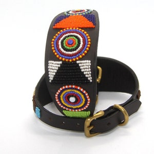 K&ouml;nnte beinhalten: Ein schwarzes Lederhundekragen mit einem bunten Perlenmuster mit geometrischen Formen und Kreisen. Das Halsband hat eine Messing-Schnalle.