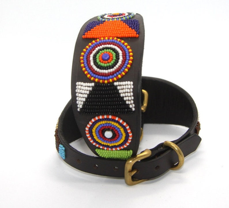 K&ouml;nnte beinhalten: Ein schwarzes Lederhundekragen mit einem bunten Perlenmuster mit geometrischen Formen und Kreisen. Das Halsband hat eine Messing-Schnalle.