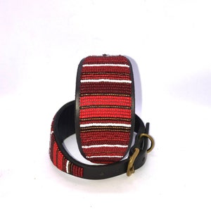 K&ouml;nnte beinhalten: Ein rotes, wei&szlig;es und braunes Perlen-Hundehalsband mit Lederbasis und einer Messing-Schnalle.