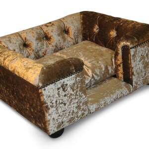 May include: A plush dog bed with a tufted headboard and a brown and gold velvet fabric. The bed has a raised edge and a lower section for a dog to rest their head.