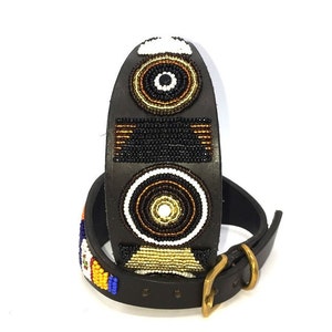 K&ouml;nnte beinhalten: Ein schwarzes Lederhundekragen mit einem Perlenmuster mit geometrischen Formen in Schwarz, Wei&szlig;, Gold und Braun.