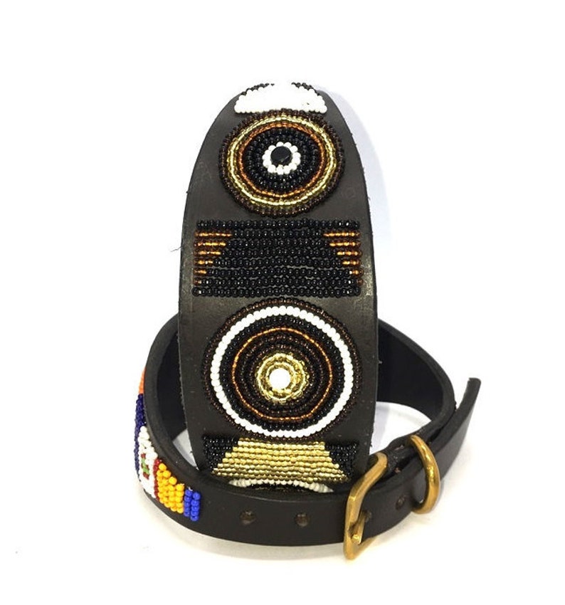 K&ouml;nnte beinhalten: Ein schwarzes Lederhundekragen mit einem Perlenmuster mit geometrischen Formen in Schwarz, Wei&szlig;, Gold und Braun.