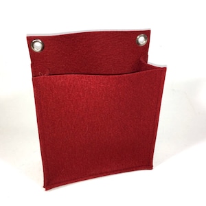 Könnte beinhalten: Rote Filz-Wandtasche mit zwei Metallösen zum Aufhängen. Die Tasche hat ein einzelnes, geteiltes Fach.