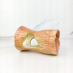 May include: A cylindrical, hollow, terracotta-colored aquarium decoration. The ornament has a textured, wood-like appearance with a large, heart-shaped opening in the center. The ends are open, and the piece is resting on a white surface.
