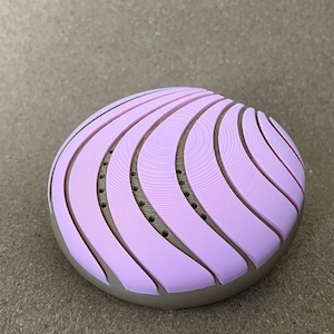 May include: A pink and brown round object with a textured surface. The object has a series of concentric circles and lines.