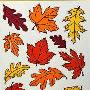 May include: A sheet of colorful fall leaf stickers. The stickers feature a variety of leaf shapes and colors, including red, orange, yellow, and brown.