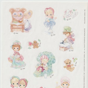 May include: A set of 10 Christmas-themed stickers featuring Precious Moments characters. The stickers depict various scenes, including a gingerbread man, a girl ice skating, a girl sweeping snow, a girl reading a book, a girl baking, a girl holding a teddy bear, a girl holding a candle, and a girl holding a book with a bird on it.