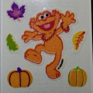 Peut inclure: Planche d'autocollants avec un personnage orange et poilu souriant et dansant, entouré d'images sur le thème de l'automne. Comprend des citrouilles, des feuilles et un petit arbre vert, sur fond blanc.