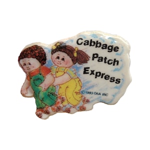 May include: A white button with a Cabbage Patch Kids design. Two Cabbage Patch Kids dolls are shown on roller skates. The text "Cabbage Patch Express" is printed on the button. The copyright information "©1983 OAA INC" is printed below the text.