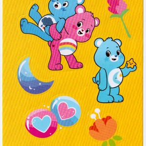 May include: A sheet of colorful stickers featuring Care Bears characters. The stickers include a pink bear with two hearts, a green bear with a four-leaf clover, a blue bear with a crescent moon, a pink bear with a rainbow, a purple bear with two lollipops, and a pink bear with a heart lock. The stickers also include a pink flower, an orange flower, and two heart-shaped bubbles.
