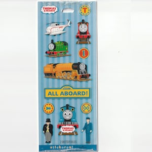 May include: A sheet of Thomas & Friends stickers featuring various train characters, a helicopter, and the text "ALL ABOARD!". The stickers are in bright colors, including red, green, and blue, with the Thomas & Friends logo at the top.