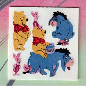 May include: A set of five Winnie the Pooh character stickers. The stickers feature Winnie the Pooh, Piglet, Eeyore, and Tigger. The stickers are printed on a white background and have a shiny, glittery finish.