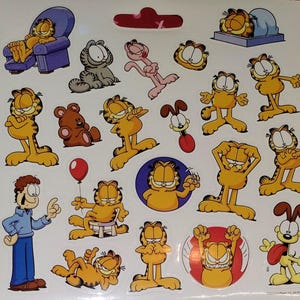 May include: Sheet of Garfield stickers featuring various poses of the orange cat, along with other characters. The stickers include Garfield in a chair, sleeping, and with Odie. The stickers are on a white background.