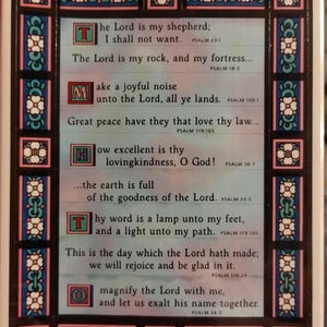 May include: A framed religious artwork with a decorative border. The artwork features several lines of text from Psalms, each starting with a large, colorful initial letter. The border is adorned with floral and geometric patterns in blue, white, and red.
