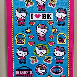 May include: A sheet of Hello Kitty stickers featuring various images of Hello Kitty in different outfits and poses. The stickers are on a blue background with yellow polka dots and include text that says "Hello Kitty" and "I ♥ HK".