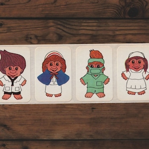 May include: Four vintage Troll doll stickers featuring healthcare professionals. Each sticker shows a different Troll doll dressed as a doctor, nurse, and surgeon, with various hair colors and outfits. The stickers are on a white rectangular sheet.