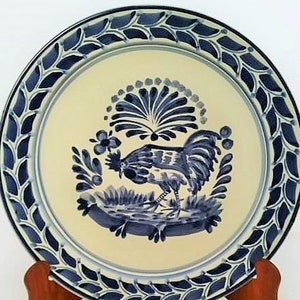 May include: A blue and white ceramic plate with a rooster design. The plate has a decorative border of blue leaves.