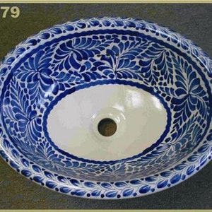 May include: Oval ceramic sink with a white interior and a blue floral pattern around the rim. The sink has a central drain hole and is decorated with intricate blue and white designs. The sink is a decorative bathroom fixture.