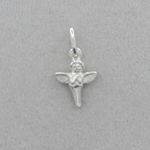 Könnte beinhalten: Ein kleiner, silberfarbener Engel-Anhänger mit ausgebreiteten Flügeln und einem Heiligenschein. Der Anhänger ist an einer kleinen Schlaufe befestigt, geeignet für eine Halskette oder ein Armband. Der Engel ist vor einem grauen Hintergrund zentriert.