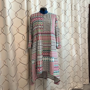 May include: A long-sleeved dress featuring a vibrant, multi-colored geometric pattern in shades of pink, green, black, and white. The garment has a high neckline and a high-low hemline, displayed on a blue adjustable dress form mannequin.