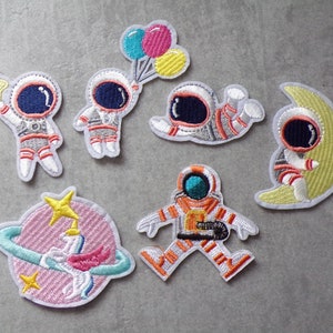 Op de afbeelding: Set van 6 geborduurde strijkpatches met astronauten, een halve maan en een planeet met een ster. De patches zijn wit met kleurrijke details.