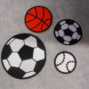 Könnte beinhalten: Vier gestickte Aufnäher mit verschiedenen Sportbällen: ein Basketball, ein Fußball, ein Fußball und ein Baseball. Die Aufnäher sind alle weiß mit schwarzen Nähten und befinden sich auf einem grauen Hintergrund.