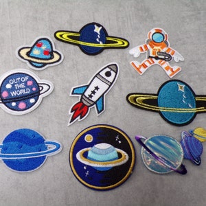 Könnte beinhalten: Ein Set mit zehn gestickten Bügelbildern mit Weltraummotiven. Die Patches zeigen Planeten, eine Rakete, einen Astronauten und die Worte "Out of the World".