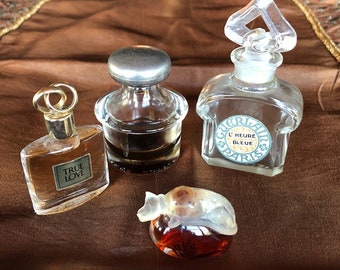 Puede incluir: Cuatro frascos de perfume en miniatura, dos frascos de vidrio transparente con tapas plateadas, un frasco de vidrio transparente con una tapa dorada y un frasco de vidrio transparente con un líquido rojo en su interior. Los frascos están sobre una superficie marrón.